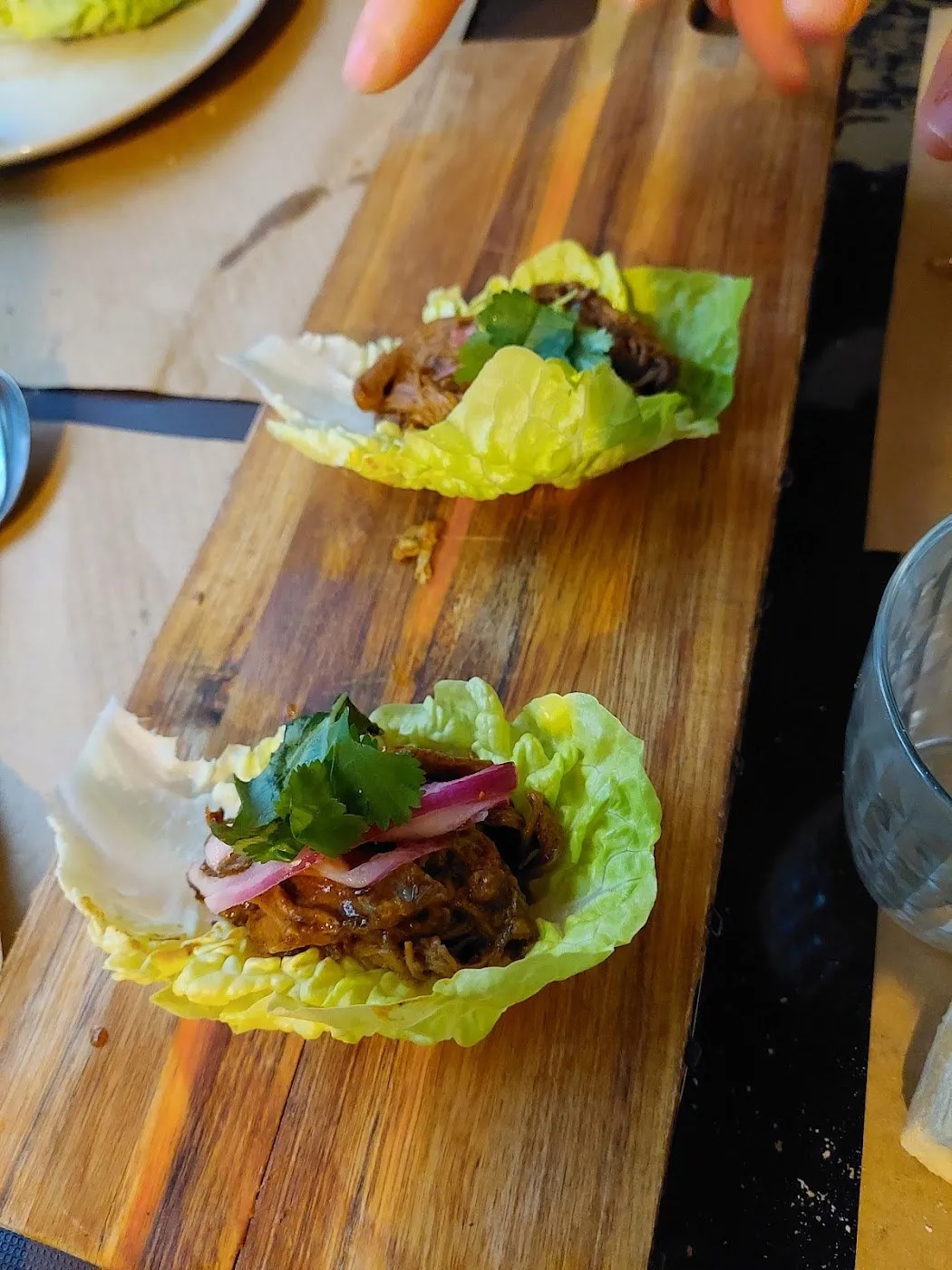 Dos hojas de lechuga con carne deshilachada y cebolla encurtida sobre una tabla
